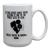 White 15oz ceramic drinking mug with the saying, "Getting kissed while you're sleeping is one of the purest acts of love....unless you're in prison."
